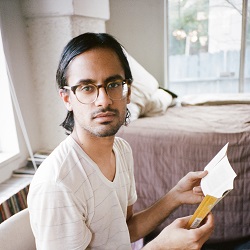 Photo of Prabjit holding a cassette insert on a chair in a room with many tapes, CDs, and vinyl